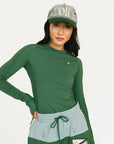 Person wearing a green Marie long-sleeve shirt and light blue shorts with a cap on a white background