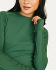 Person wearing a green Marie long-sleeve shirt and light blue shorts with a cap on a white background