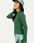 Person wearing a green Marie long-sleeve shirt and light blue shorts with a cap on a white background