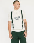 A man wearing a beige zip sweater with vertical green stripes and the text 'Fore All x Khalhon' on the chest, paired with dark green shorts.