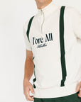 A man wearing a beige zip sweater with vertical green stripes and the text 'Fore All x Khalhon' on the chest, paired with dark green shorts.
