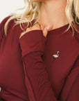 Woman wearing a burgundy Marie Long Sleeve with a logo on a white background