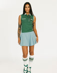 Woman wearing a green sleeveless top and light blue skirt with white sneakers on a white background
