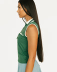 Woman wearing a green sleeveless top with white trim on a plain background