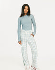 Woman wearing a light blue long-sleeve top and green plaid pants on a white background