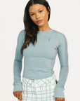 Woman wearing a smoke blue Marie long-sleeve top and plaid pants on a white background