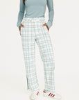 Person wearing a light blue long-sleeve top and plaid pants with white sneakers on a white background