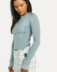 Woman wearing a smoke blue Marie long-sleeve top and plaid pants on a white background