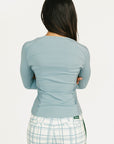 Woman wearing a smoke blue Marie long-sleeve top and plaid pants on a white background
