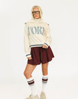 Person wearing a cream hoodie with 'FORE' text and maroon shorts on a white background