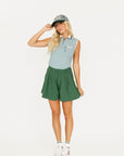 Person wearing a smoke blue sleeveless Annie Polo and a green Eleanor short on a plain background