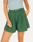 Person wearing a smoke blue sleeveless Annie Polo and a green Eleanor short on a plain background