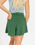 Person wearing a smoke blue sleeveless Annie Polo and a green Eleanor short on a plain background
