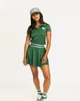 Woman wearing a green Brooklyn Polo and Brooklyn Skirt and a University Hat with visible branding on a white background