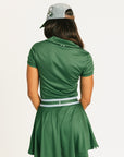Woman wearing a green Brooklyn Polo and Brooklyn Skirt and a University Hat with visible branding on a white background