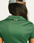 Woman wearing a green Brooklyn Polo and Brooklyn Skirt and a University Hat with visible branding on a white background