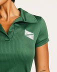 Woman wearing a green Brooklyn Polo and Brooklyn Skirt and a University Hat with visible branding on a white background
