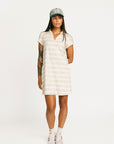 Woman wearing a Fore All Poppy white striped dress and cap on a plain background