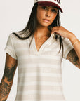 Woman wearing a Fore All Poppy white striped dress and cap on a plain background