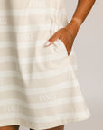 Woman wearing a Fore All Poppy white striped dress and cap on a plain background