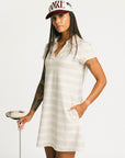 Woman wearing a Fore All Poppy white striped dress and cap on a plain background