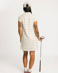 Woman wearing a Fore All Poppy white striped dress and cap on a plain background