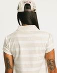 Woman wearing a Fore All Poppy white striped dress and cap on a plain background