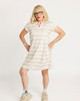 Woman wearing a Fore All Poppy white striped dress and cap on a plain background