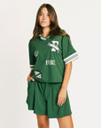Woman wearing a green Fore All Dillon Polo with visible branding on a plain background