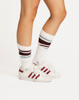 Person wearing white sneakers with red stripes and striped socks on a plain background
