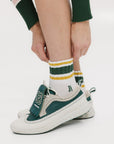 A person wearing retro ankle socks in mustard and green colors, paired with a green and white shoe.