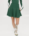 A person wearing a high-waisted green skirt with a solid pattern, paired with a white top and light-colored shoes.