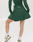 A person wearing a high-waisted green skirt with a solid pattern, paired with a white top and light-colored shoes.