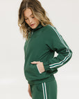 A woman wearing a green long-sleeve jacket with white stripes on the sleeves and matching green pants, standing against a white background.