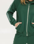 A woman wearing a green long-sleeve jacket with white stripes on the sleeves and matching green pants, standing against a white background.