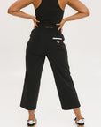 Person wearing black high-waisted pants with a white logo on a light gray background