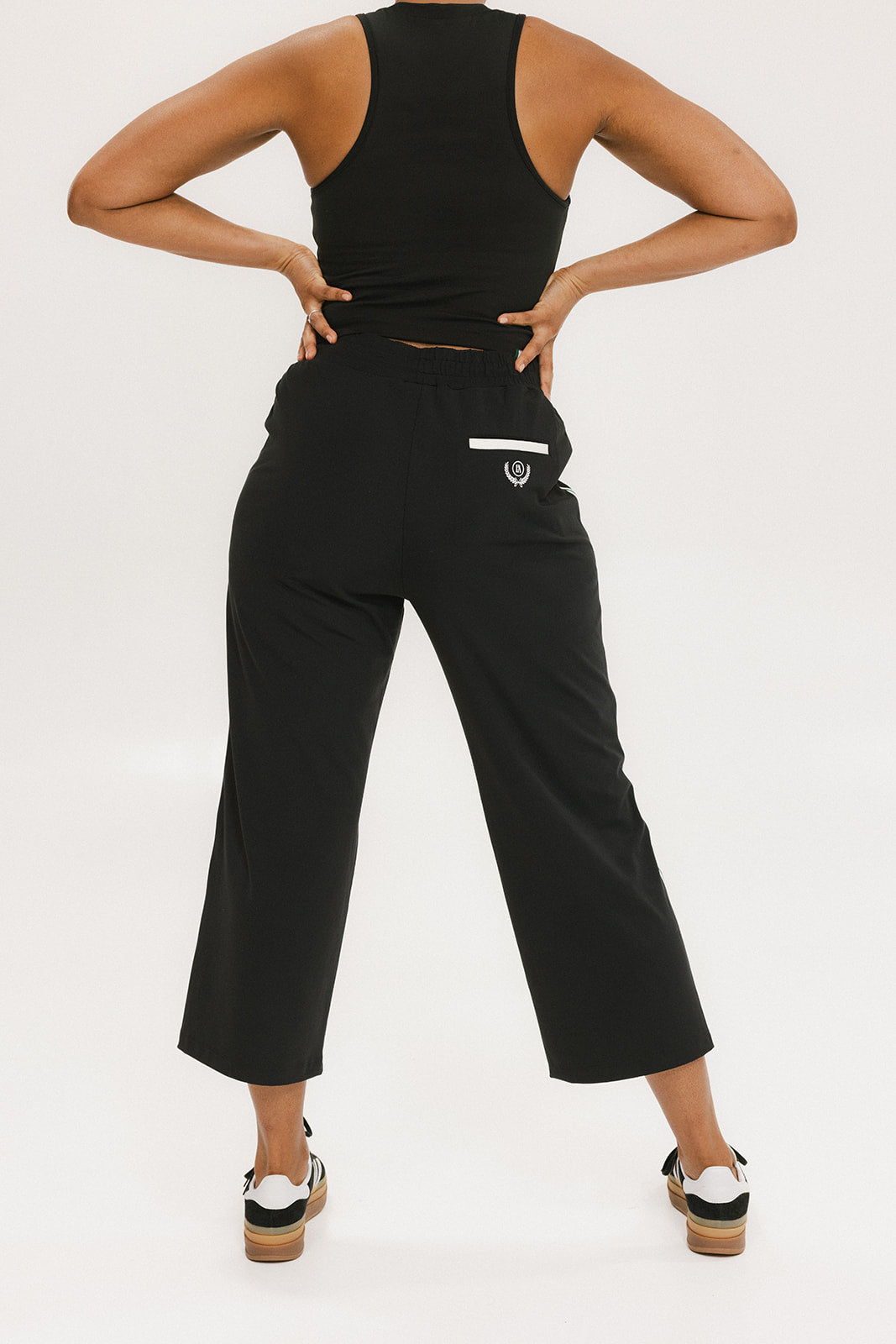 Person wearing black high-waisted pants with a white logo on a light gray background