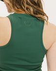 A woman wearing a green tank top with a built-in bra, paired with patterned shorts and a black cap with the text 'FORE ALL' on it.