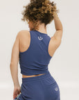 A woman wearing a sleeveless indigo tank top with built-in bra, paired with matching indigo pants.