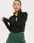 A woman wearing a black long-sleeve mock neck top with a green skirt. The top has a small logo on the neck area.