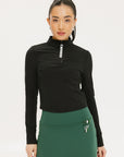 A woman wearing a black long-sleeve mock neck top with a green skirt. The top has a small logo on the neck area.