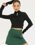 A woman wearing a black long-sleeve mock neck top with a green skirt. The top has a small logo on the neck area.