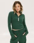 A woman wearing a green mock-neck long-sleeve golf top and matching pants, standing with hands in pockets.