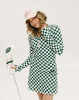 A person wearing a green and white checkered mock-neck long-sleeve golf top and matching golf skort, holding a golf club.