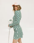 A person wearing a green and white checkered mock-neck long-sleeve golf top and matching golf skort, holding a golf club.
