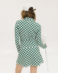 A person wearing a green and white checkered mock-neck long-sleeve golf top and matching golf skort, holding a golf club.