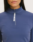 A woman wearing a blue mock-neck long-sleeve top.