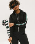 A person wearing a black jacket with green and white stripes on the sleeves, holding a black and white striped object.