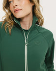 A woman wearing a green long-sleeve jacket with white stripes on the sleeves and matching green pants, standing against a white background.