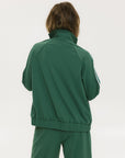 A woman wearing a green long-sleeve jacket with white stripes on the sleeves and matching green pants, standing against a white background.